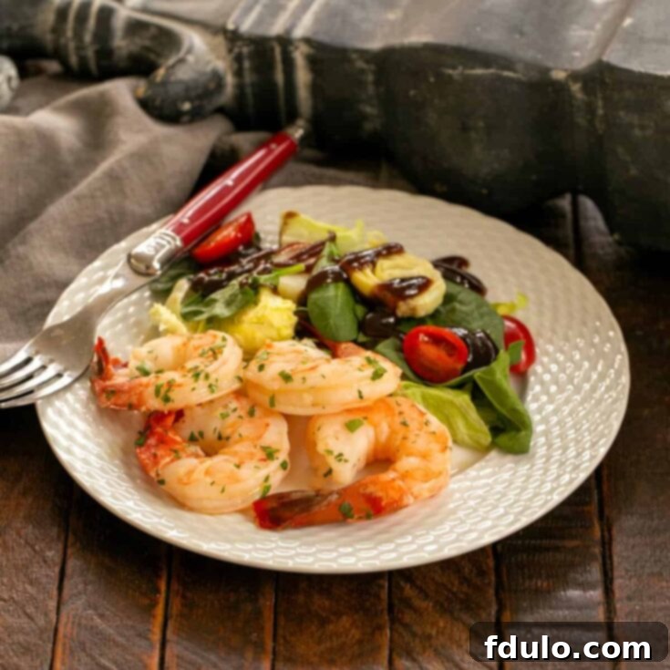 Shrimp scampi on a white dinner plate with salad and fork, showcasing the finished dish.