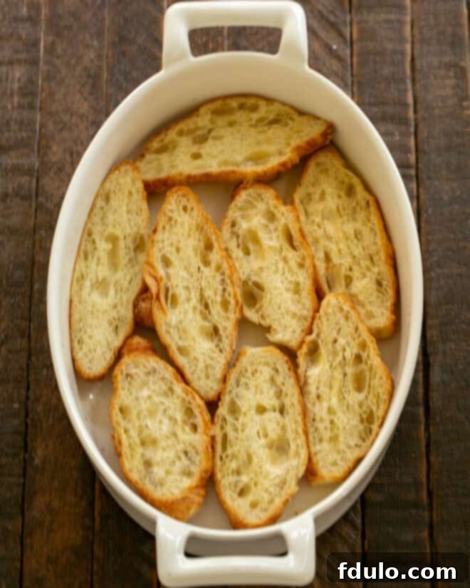 Flaky Croissant French Toast with Fresh Raspberries 5 Mini croissants cut in half lengthwise, showing their flaky layers, precisely arranged cut-side up in a buttered square baking dish, ready for filling.