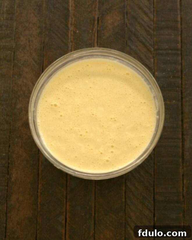 Flaky Croissant French Toast with Fresh Raspberries 7 A bowl containing ingredients for the egg custard, including granulated sugar, remaining cream cheese, half-and-half, eggs, salt, lemon juice, and vanilla, being thoroughly whisked to create a smooth, unified liquid.