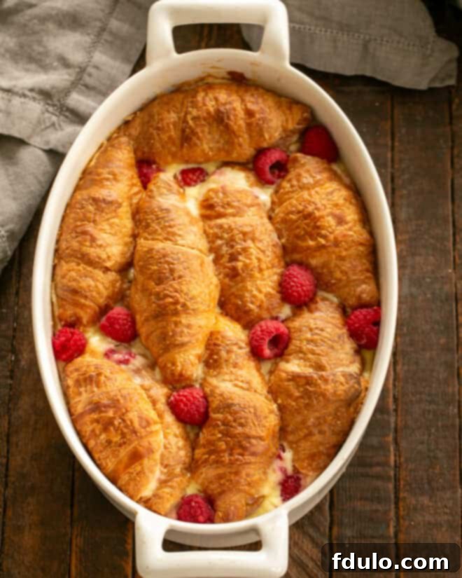 Flaky Croissant French Toast with Fresh Raspberries 9 A freshly baked Croissant French Toast Casserole, golden brown and perfectly puffed, cooling slightly in the baking dish after being dusted with powdered sugar, ready to be served.