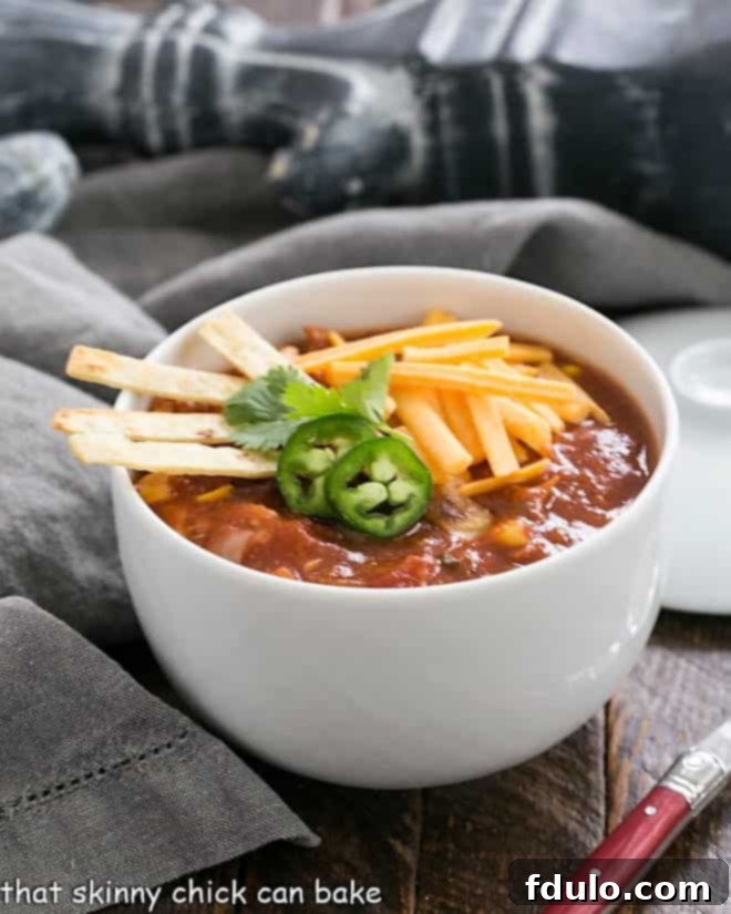 Fiesta Chicken Tortilla Soup 3 A side view of a white bowl filled with richly colored tortilla soup, artfully topped with fresh garnishes.