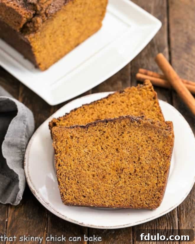 Best pumpkin bread recipe with a sweet dusting of cinnamon sugar on the top crust Exquisitely sliced pieces of pumpkin bread beautifully arranged on a round white plate, accompanied by fragrant cinnamon sticks for a charming presentation.