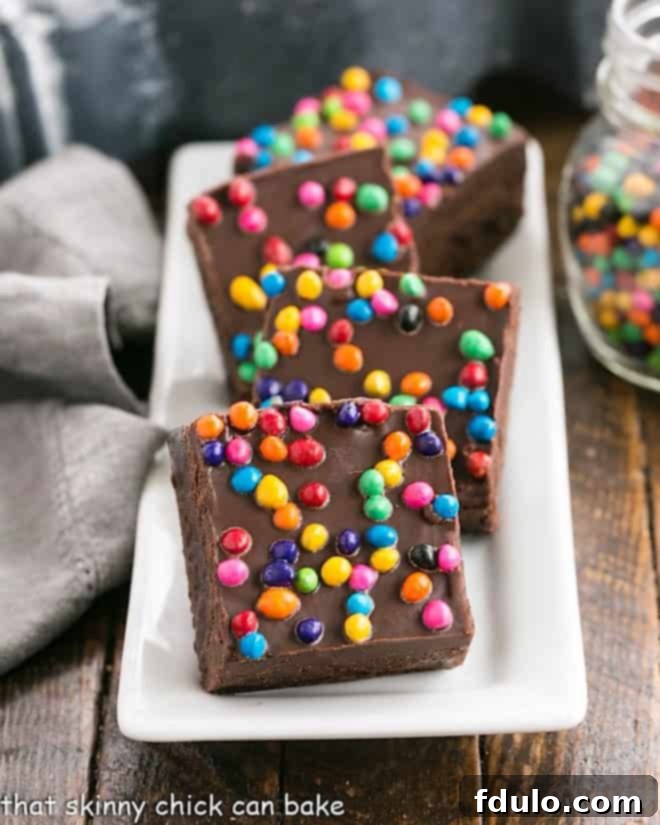 A tray of freshly baked Cosmic Brownies, rich and fudgy, topped with ganache and vibrant rainbow sprinkles, ready to be sliced and enjoyed.