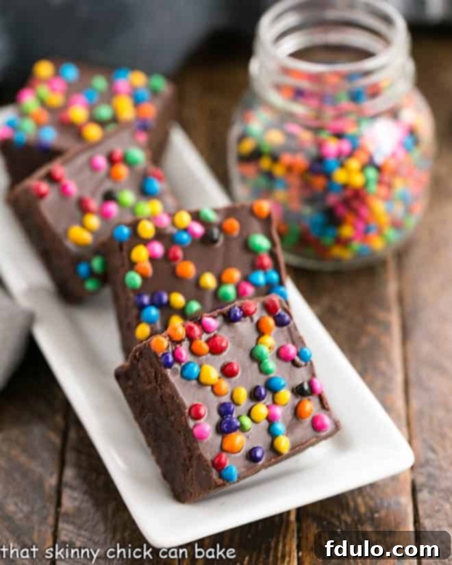 A baking tray filled with delectable Cosmic Brownies, alongside a jar brimming with colorful rainbow chip sprinkles, ready for the final touch.