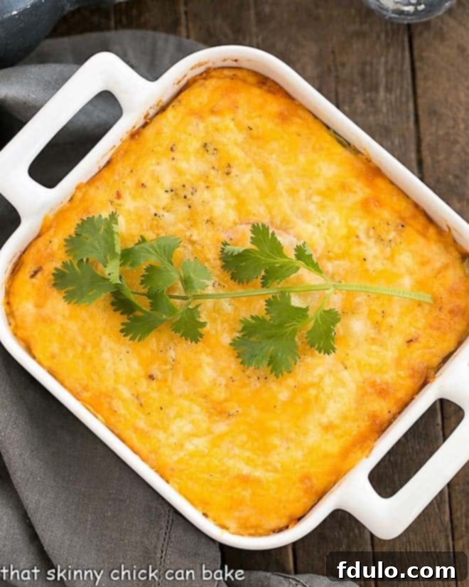Chili Relleno Casserole - Layers of gooey cheese, eggs, tomatoes, and mild peppers create an irresistible Tex-Mex dish! A square white baking dish filled with a golden, bubbling Chili Relleno Casserole, showcasing its rich, baked texture.