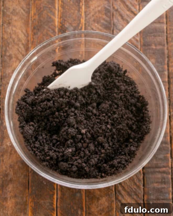 Step-by-step image showing chocolate cookie crumbs being mixed with melted butter in a bowl, before being pressed into a prepared pan.