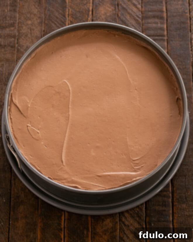 Step-by-step image showing the chocolate mousse filling being scraped into the prepared cookie crust in a springform pan and the top being smoothed.