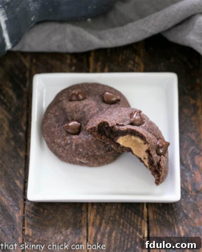 A square white plate holding two delicious chocolate peanut butter cookies, one broken in half to reveal the creamy peanut butter filling inside.