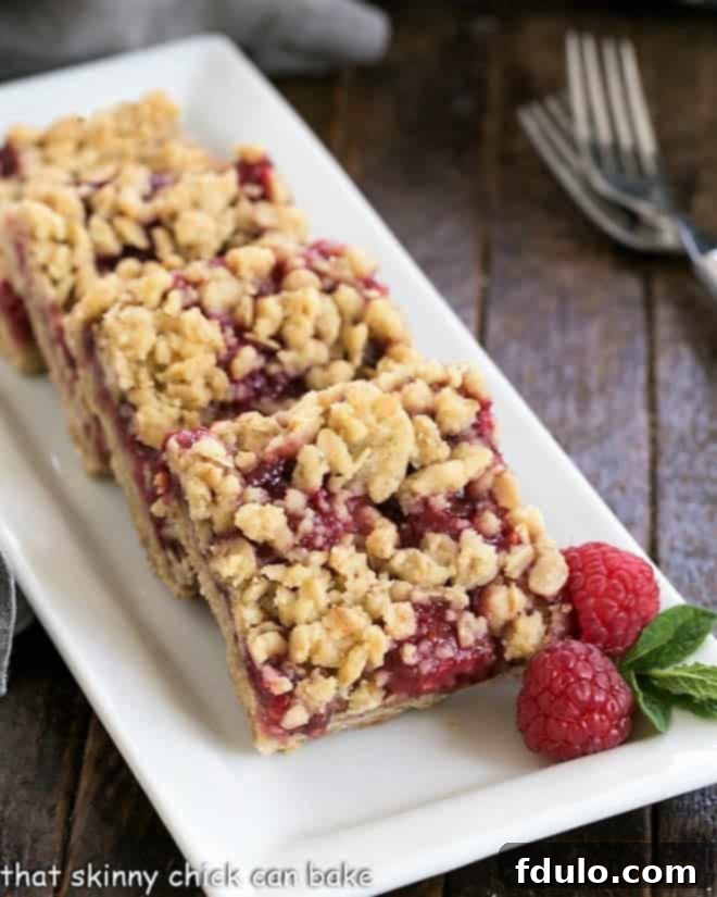 Two golden brown Raspberry Streusel Bars on a white serving tray, garnished with fresh raspberries and mint sprigs.