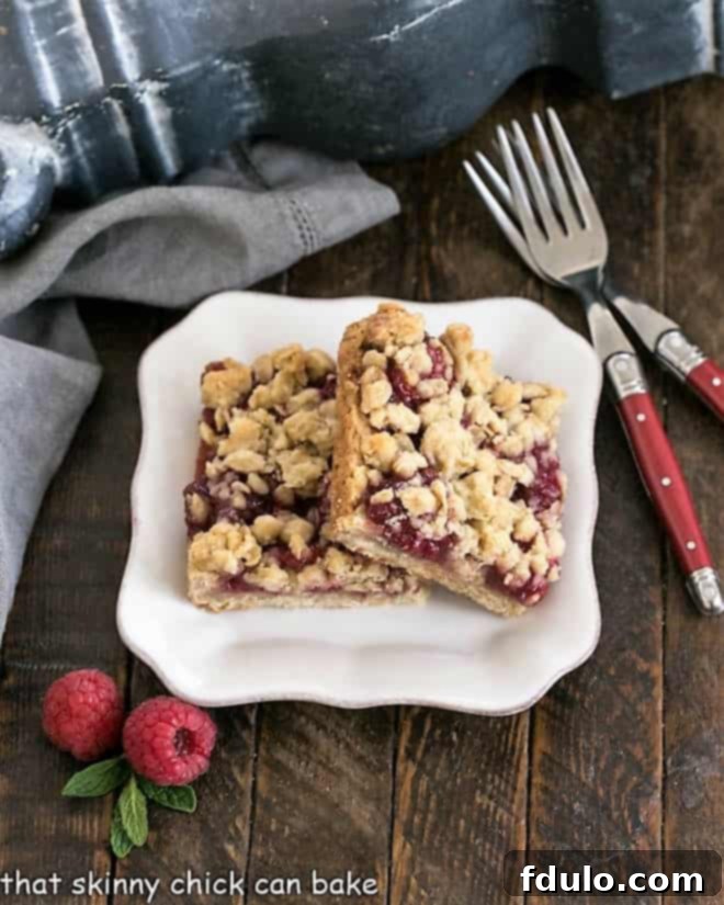 Two perfect Raspberry Crumble bars on a white dessert plate with two elegant red-handled forks, ready to be enjoyed.