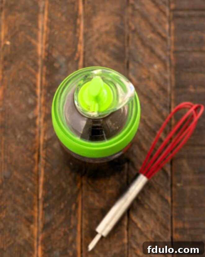 Spinach salad dressing in a carafe with a small whisk.