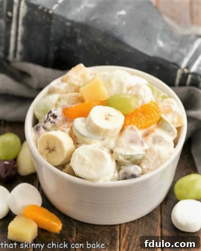 A festive Holiday Fruit Salad with Marshmallows in a pristine white ceramic bowl, surrounded by colorful fresh fruits like grapes and oranges, and scattered marshmallows, highlighting its visual appeal for any celebration.