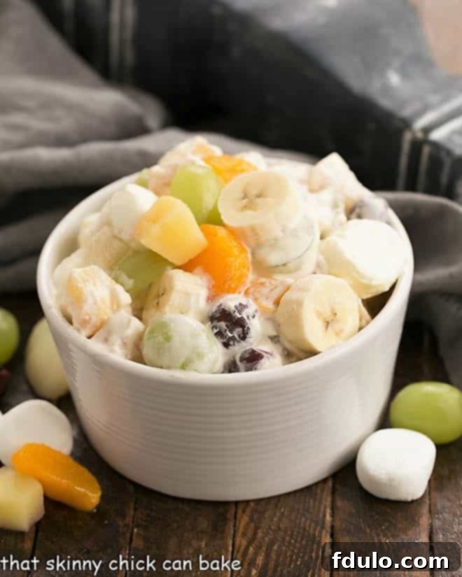 A festive 24-hour fruit salad presented in an elegant white bowl, beautifully garnished with fresh fruit and soft marshmallows, highlighting its creamy texture and vibrant colors.