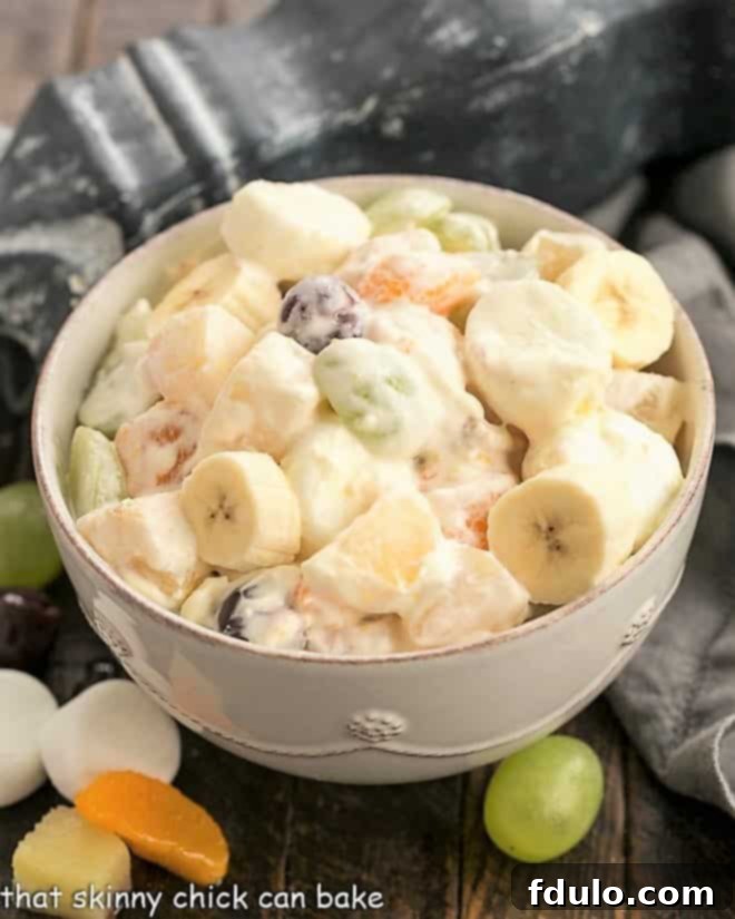 A beautifully presented holiday fruit salad in a pristine white serving bowl, garnished with a few fresh berries and mint leaves, ready for a festive table.