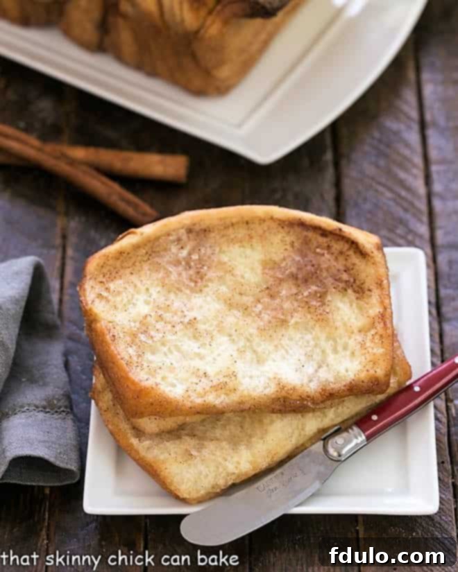 Two soft, layered slices of Cinnamon Pull Apart Bread on a square white plate, with a small silver knife resting beside them.
