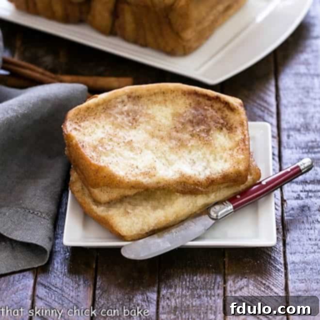 Two slices of cinnamon pull apart bread on a white plate with a red handle knife, showcasing the fluffy, sweet layers of the coffee cake.