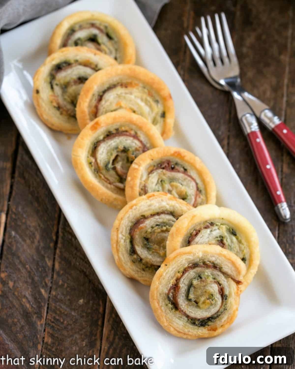 Prosciutto, Gruyere and Basil Pinwheels - an easy, elegant puff pastry appetizer that's a breeze to prepare Overhead view of Prosciutto, Gruyere and Basil Pinwheels on a rectangular white ceramic tray.