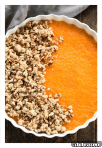 Praline topping being sprinkled over the sweet potato casserole base, showing a partial layer.