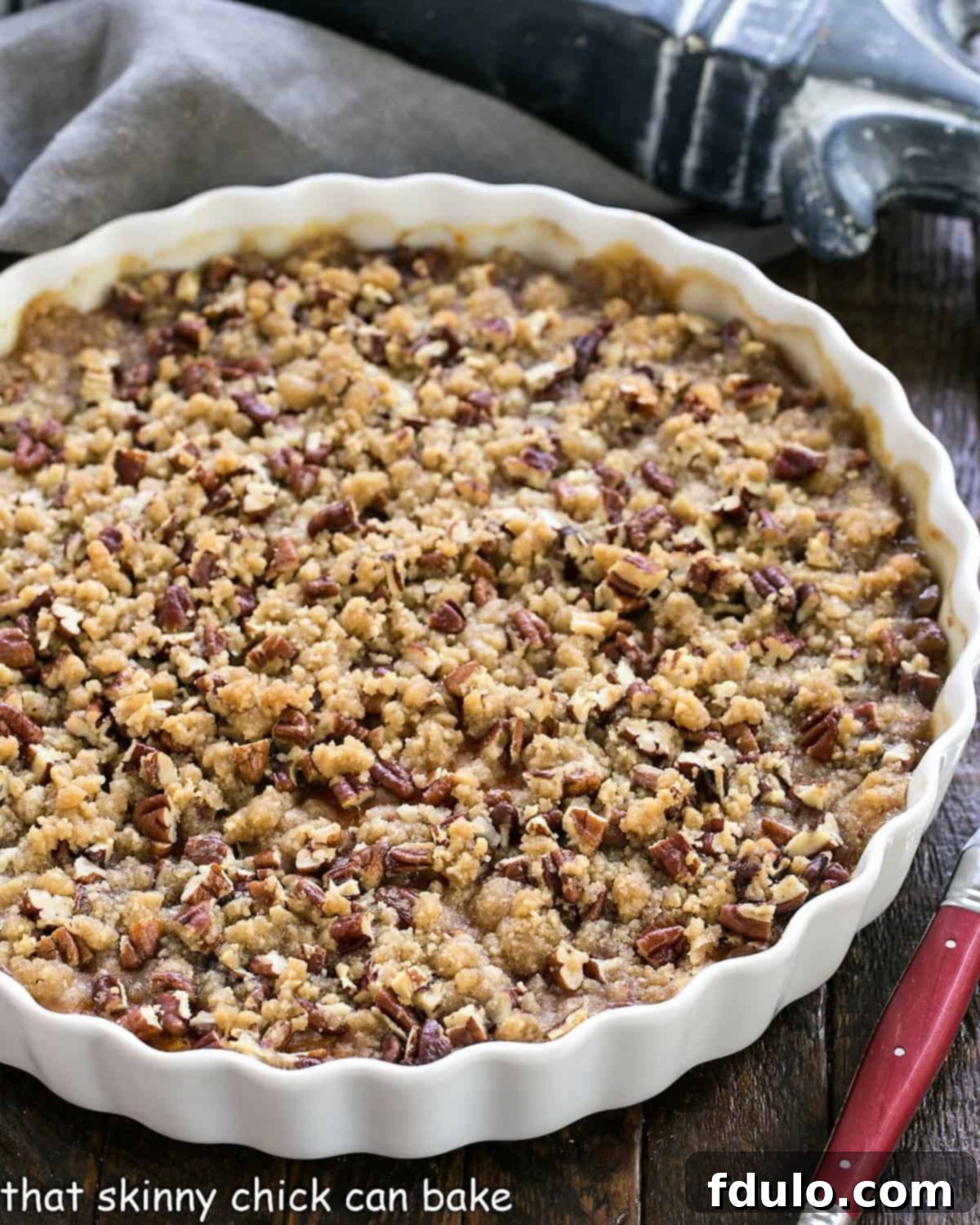 Overhead view of a perfectly baked Praline Topped Sweet Potato Casserole in a beautiful white, round baking dish, adorned with a festive arrangement.
