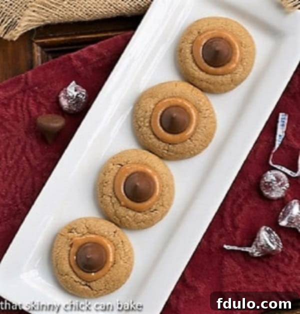 An overhead shot showcasing a rectangular white tray filled with perfectly baked Caramel Biscoff Blossoms, each featuring a golden cookie base, a glistening caramel pool, and a classic Hershey's Kiss. Ideal for gifting or dessert platters.