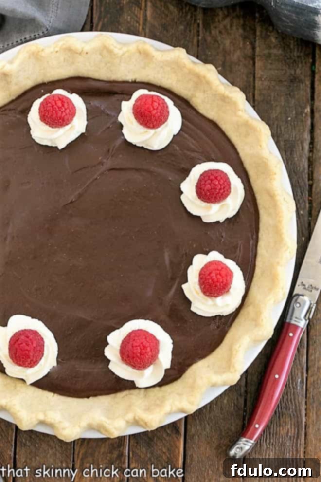 Overhead view of a chocolate cream pie with a red handled knife.