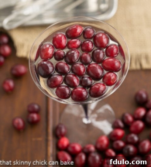 Two White Cosmopolitans in martini glasses garnished with fresh cranberries.