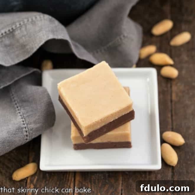 Two perfectly cut slices of layered chocolate peanut butter fudge, neatly stacked on a square white plate, ready for serving.