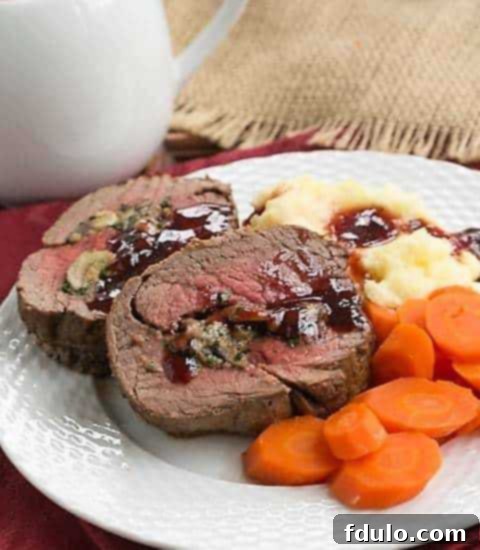 Gorgonzola and Mushroom Stuffed Beef Tenderloin - An elegant, celebratory entree you can make at home! Gorgonzola Mushroom Stuffed Beef Tenderloin with red wine sauce on a white dinner plate, ready to be served