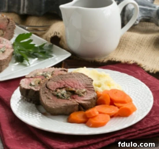 Gorgonzola and Mushroom Stuffed Beef Tenderloin - An elegant, celebratory entree you can make at home! Gorgonzola and Mushroom Stuffed Beef Tenderloin on a dinner plate with roasted carrots and creamy mashed potatoes, ready for a festive meal.