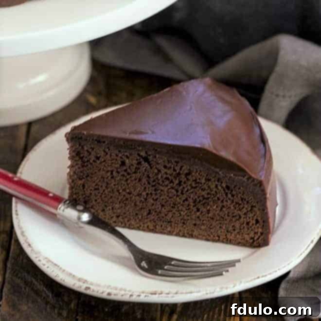 A slice of the One Layer Fudge Cake on a pristine white round plate, accompanied by a festive red-handled fork. This dessert is rich, delectable, and the perfect chocolate cake recipe for smaller gatherings.