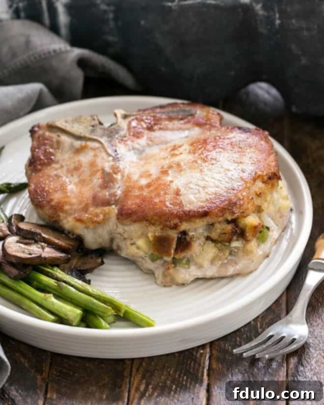 A perfectly cooked Stuffed Pork Chop on a white dinner plate, accompanied by vibrant asparagus and earthy mushrooms.
