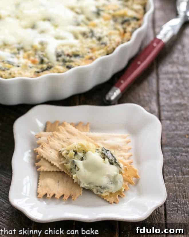 A spoonful of Hot Spinach and Artichoke Dip served on an appetizer plate with golden crackers.