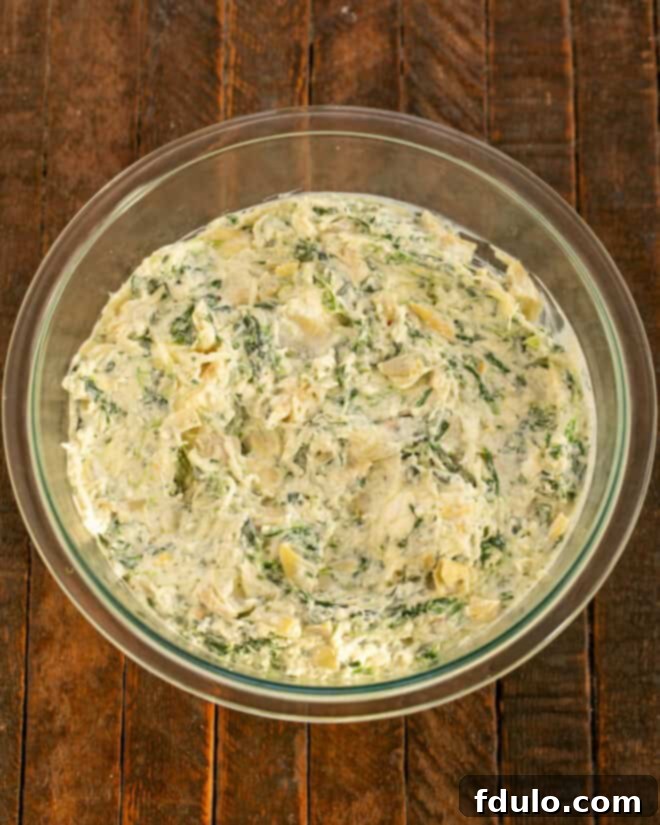 Mixed spinach artichoke dip ingredients in a mixing bowl, showing creamy texture.