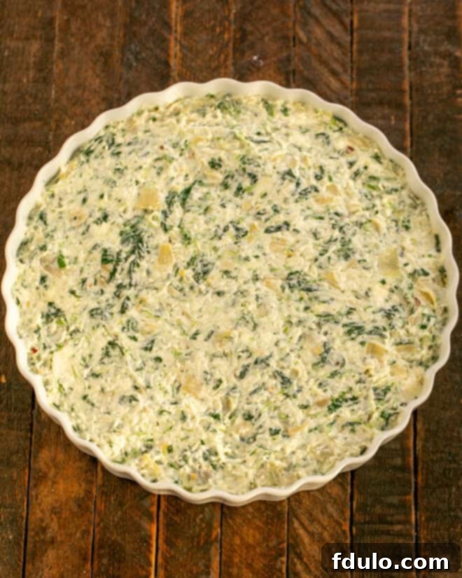 Spinach artichoke dip spread evenly in a baking dish, ready for the oven.