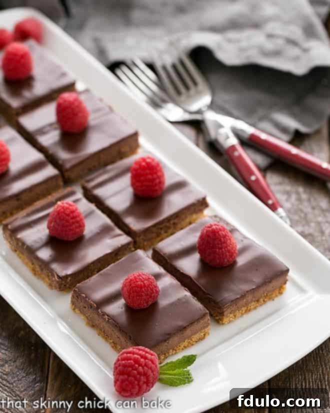 A stunning arrangement of Dark Chocolate Dessert Bars on a white tray, elegantly garnished with vibrant fresh raspberries and sprigs of mint, ready to be served.