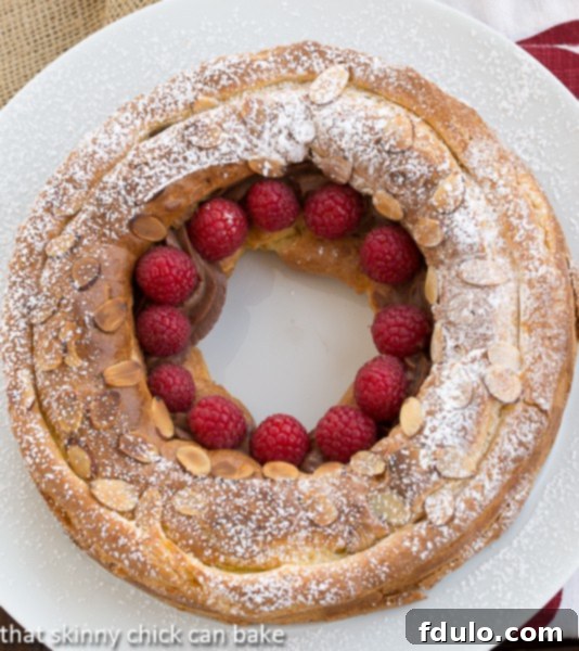 Overhead view of a Paris brest on a white serving plate garnished with raspberries.