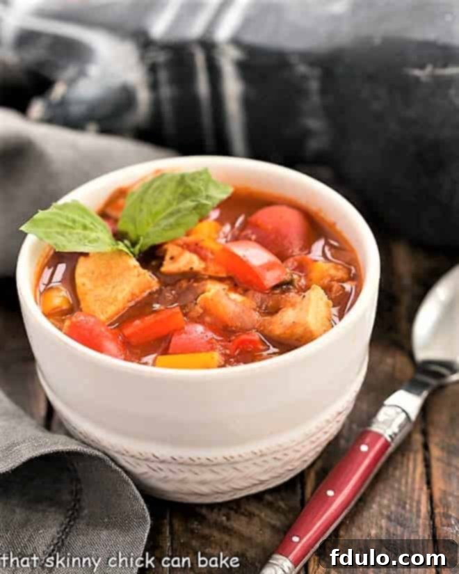 The ultimate chicken chili recipe - This unique, pepper-forward chicken chili is a proven crowd-pleaser, ideal for game day gatherings or any occasion calling for a comforting and hearty meal. A close-up of Chicken and Bell Pepper Chili in a pristine white bowl, garnished with vibrant fresh basil leaves.