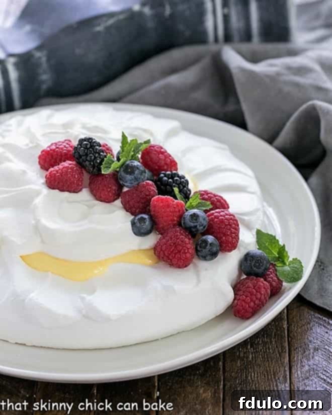Lemon Pavlova on a white serving plate garnished with fresh berries and mint leaves