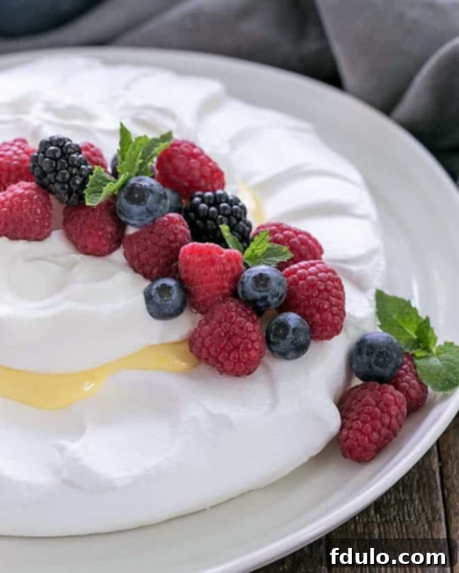 Lemon Pavlova on a white serving plate garnished with berries and fresh mint