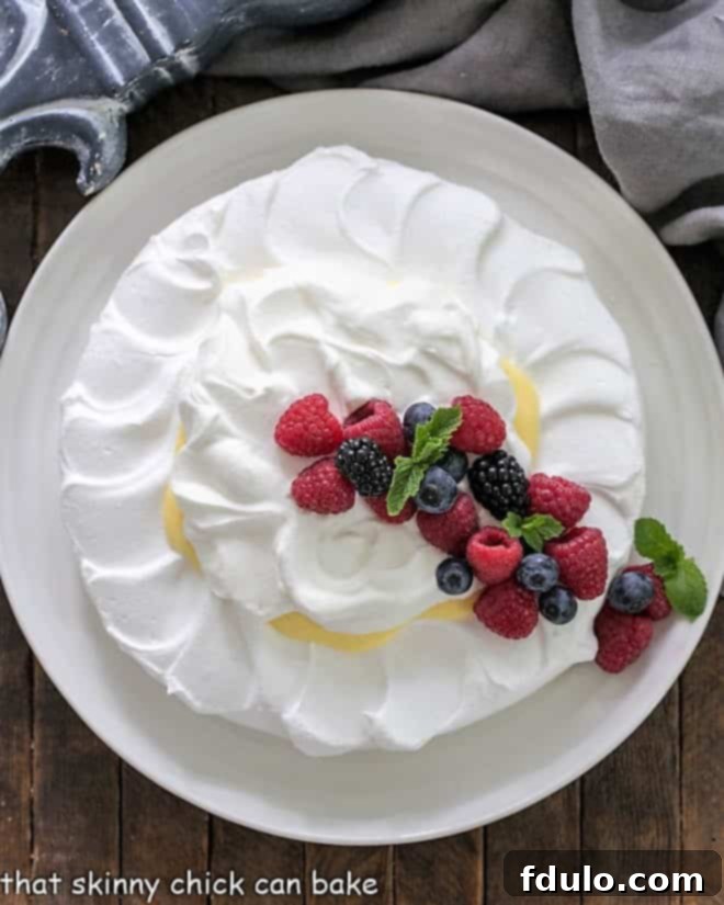 Overhead view of a pavlova dessert topped with lemon cream, whipped cream, and fresh berries, ready to be served