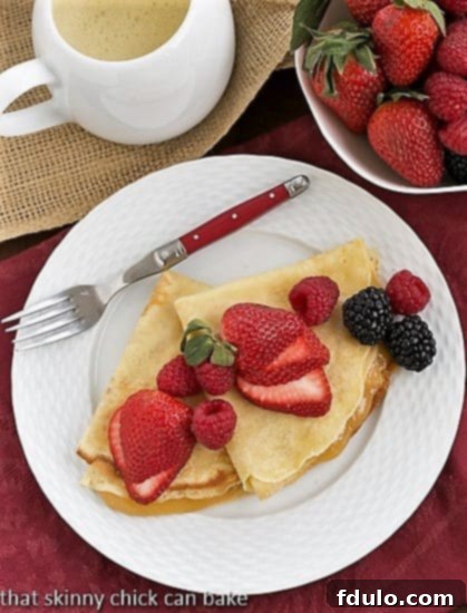 Overhead view of two folded Butter and Rum Crêpes, filled with lemon curd, on a white plate with a red handled fork, ready to be enjoyed.