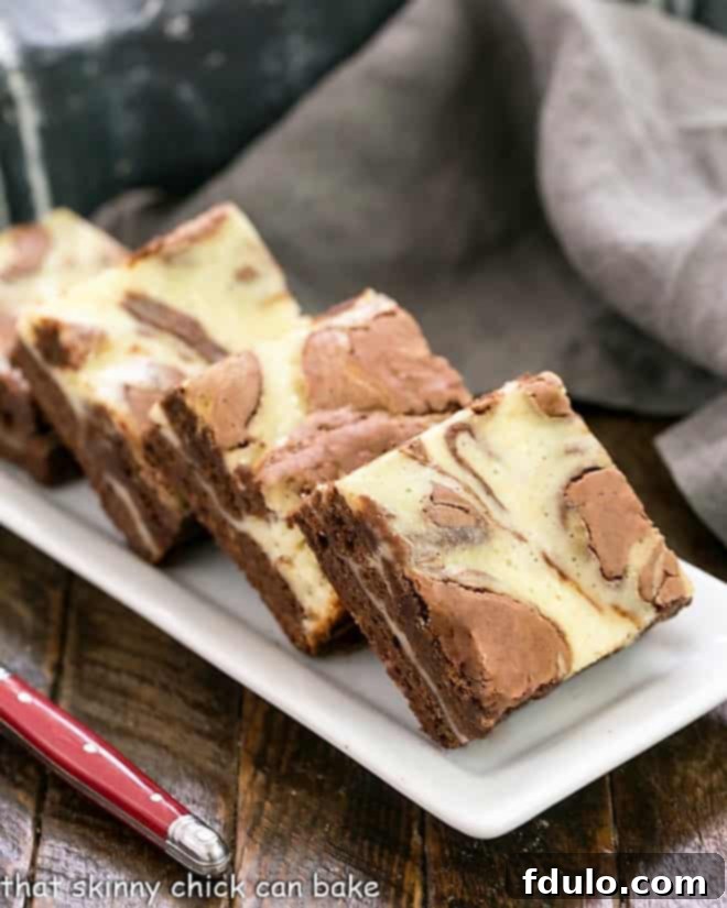 Cheesecake Swirl Brownies lined up on a white ceramic tray with a red handle fork