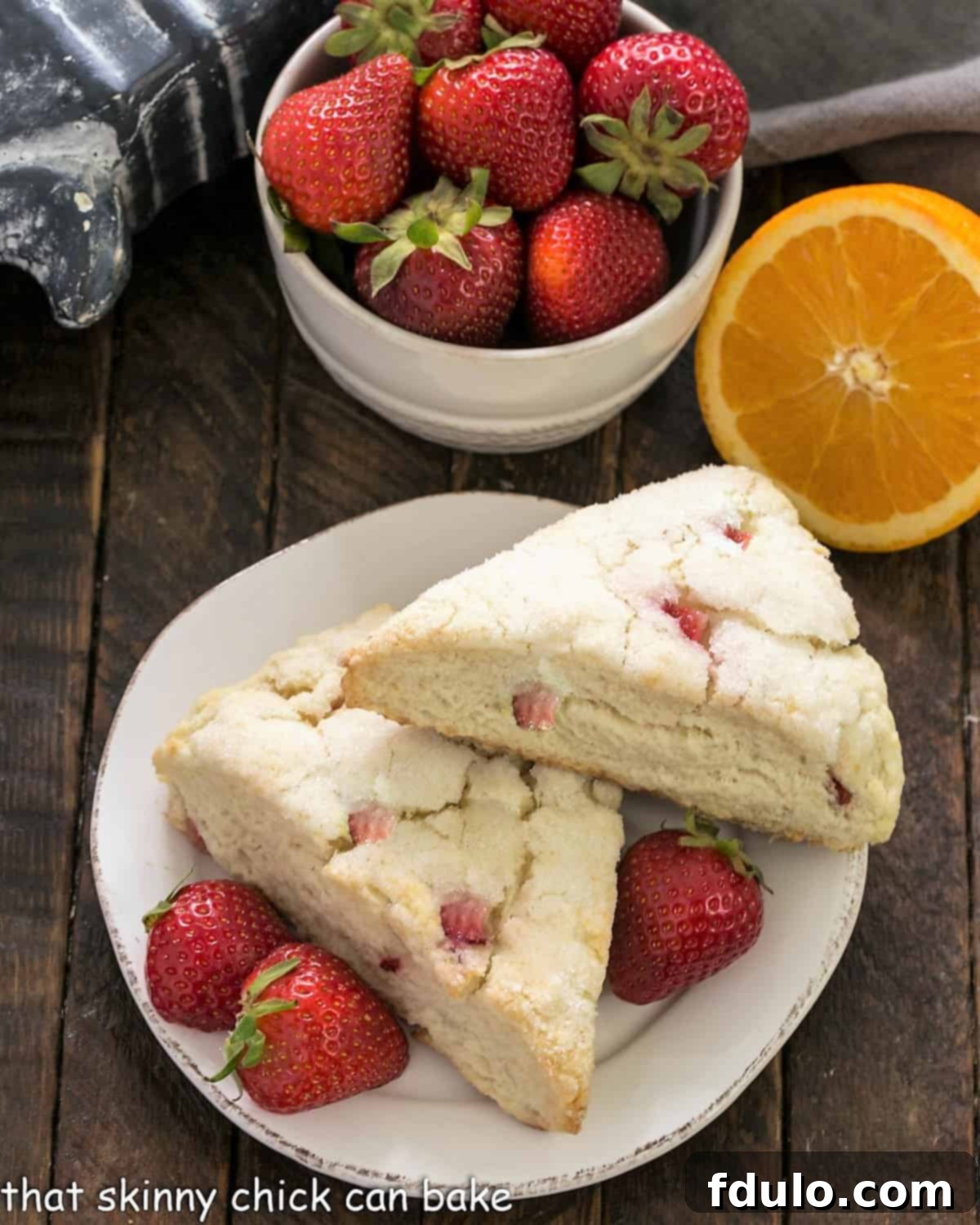 An overhead shot showcasing two perfectly baked Strawberry Buttermilk Scones on a small white plate, accompanied by fresh, ripe strawberries, highlighting their tempting texture.