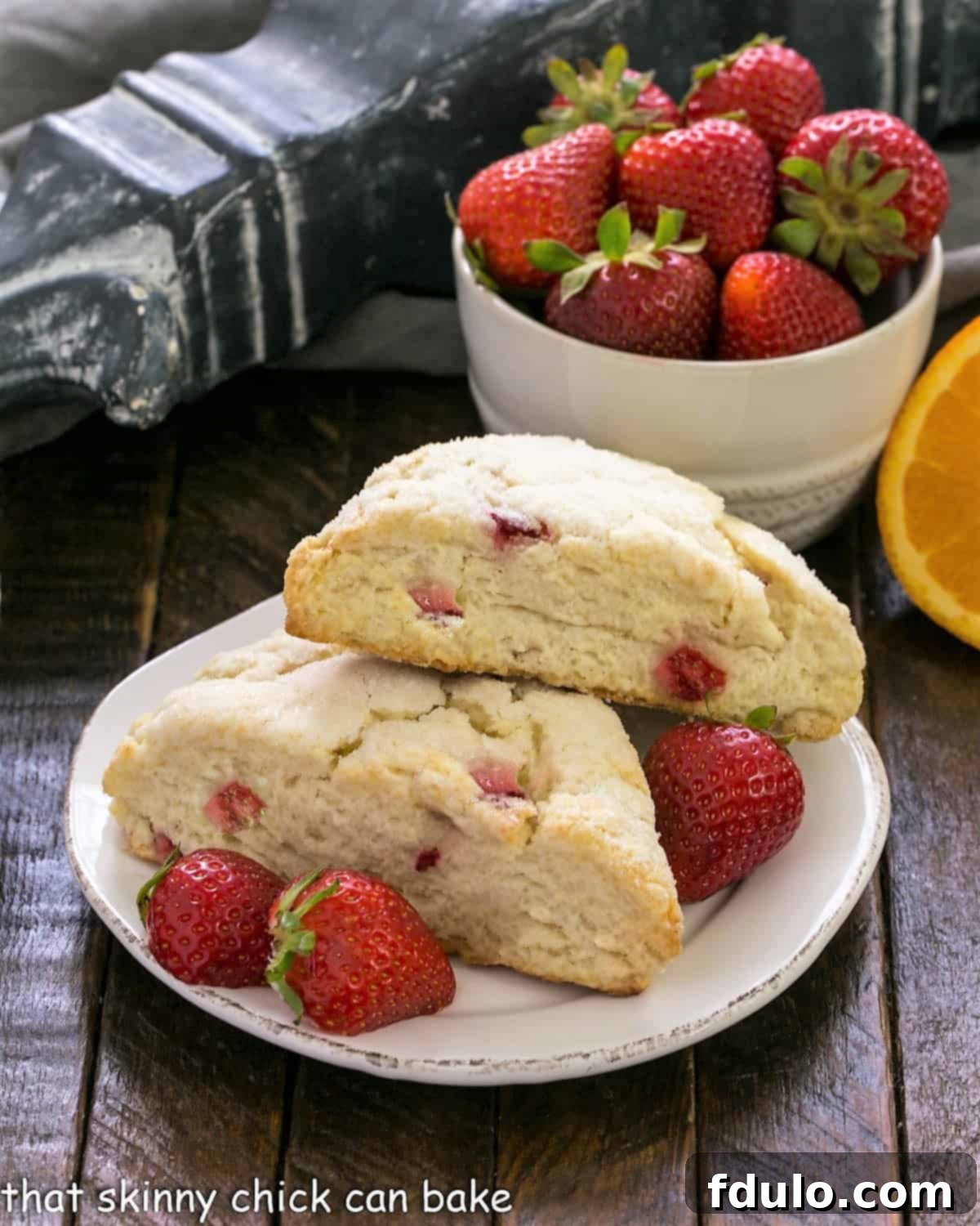 Two Strawberry Buttermilk Scones on a pristine round white plate, artfully arranged with fresh strawberries, inviting a delightful indulgence.