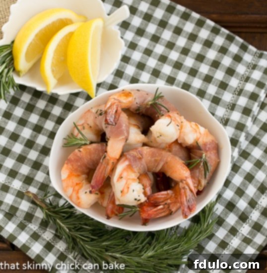 Rosemary Prosciutto Shrimp: Succulent, jumbo shrimp wrapped in prosciutto and flavored with rosemary and Sambuca! Rosemary Prosciutto Shrimp overhead view in a white bowl, showing a portion ready to be served, garnished with fresh herbs.