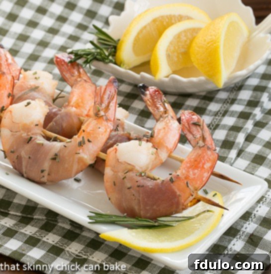 Pan-Seared Rosemary Prosciutto Shrimp 2 Rosemary Prosciutto Shrimp on a white platter, garnished with fresh rosemary and lemon wedges.