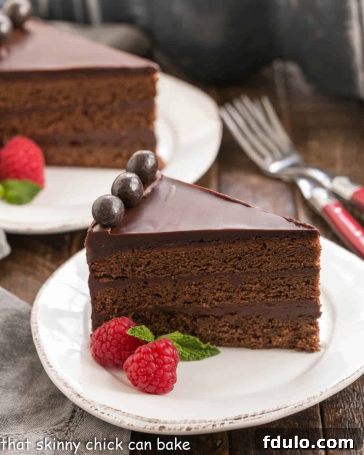 A perfectly sliced piece of Mocha Brownie Cake on a pristine white dessert plate, revealing its three distinct layers and generous ganache frosting. Another slice sits invitingly in the background.