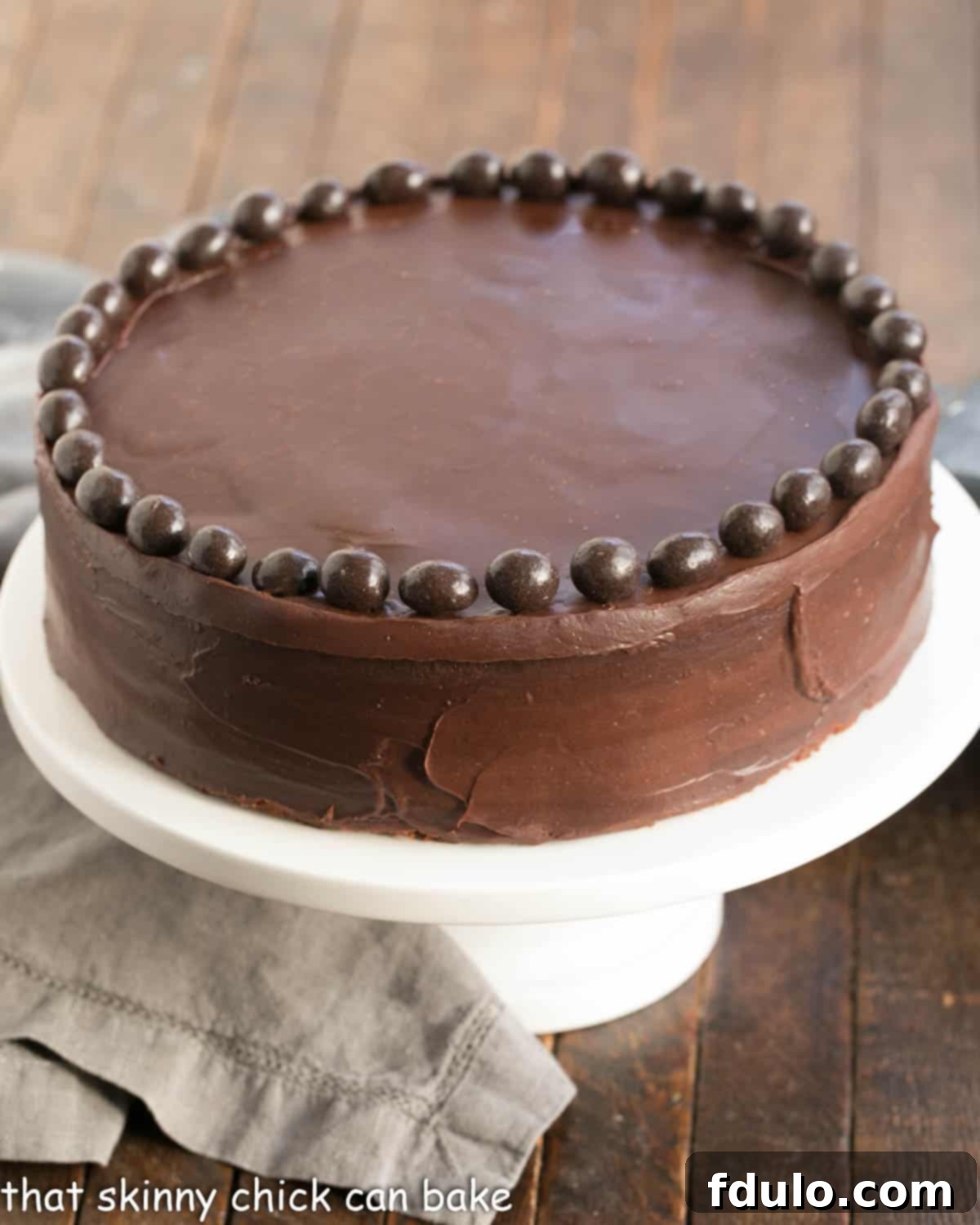 A beautifully presented Mocha Brownie Cake on a pristine white ceramic cake stand, ready to be served. The glossy ganache frosting gleams under the light.