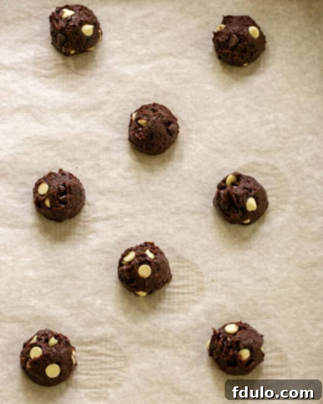 Scooping brownie cookie dough onto a parchment-lined baking sheet.