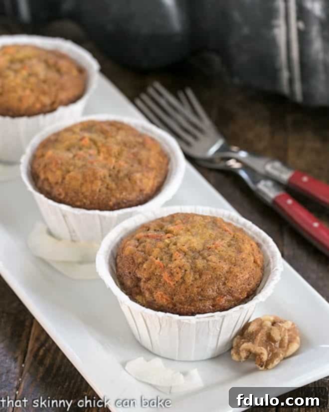 Two Cream Cheese Filled Carrot Cake Muffins in white paper liners on a white platter, showcasing their golden-brown tops and inviting texture.